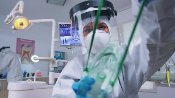 Tandarts in coverall leunend over patiënt zetten oxigen masker — Stockvideo