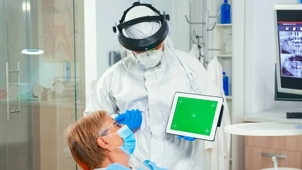 Dentista em macacão apontando para tela verde na unidade odontológica — Fotografia de Stock