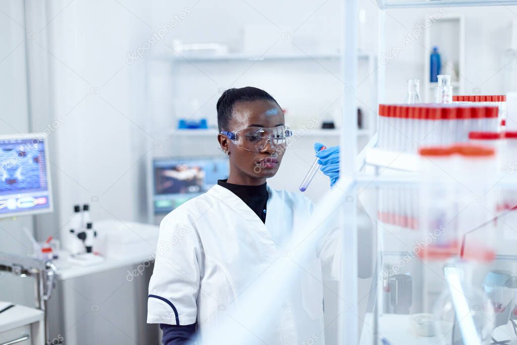 African scientist in protective glasses looking at test tube