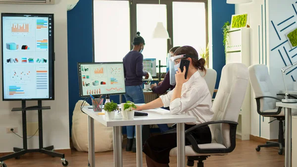 Freelancer met masker praten op mobiele telefoon in fron van de computer — Stockfoto