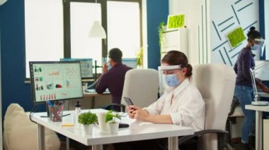 Maskeli bir iş kadını ofis odasında telefonla konuşuyor.