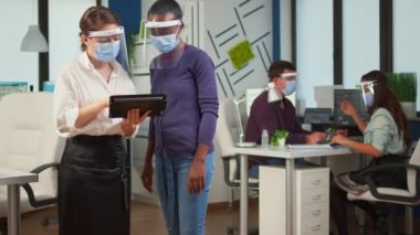 Yüz maskeli bir işçi elinde tablet olan siyah bir kadınla tartışıyor.