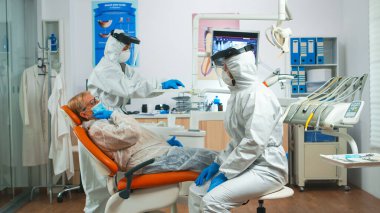 Kadın diş sorununu koruma kıyafeti giyen doktora anlatıyor.