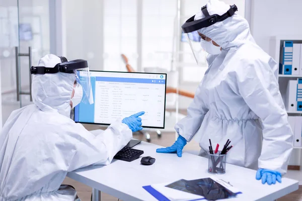 Dentist assistant in ppe suit pointing at patient waiting list