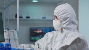 Koruyucu kıyafetli bilim adamının bilgisayarda daktilo etmesi.