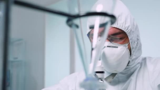Биохимик в костюме ppe смотрит в микроскоп во время эксперимента — стоковое видео