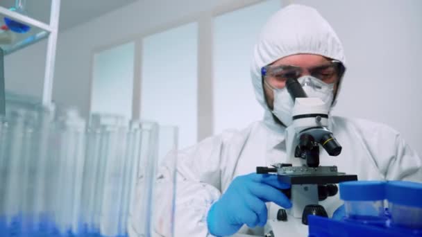 Científico en traje de ppe llevando a cabo el experimento con microscopio — Vídeos de Stock