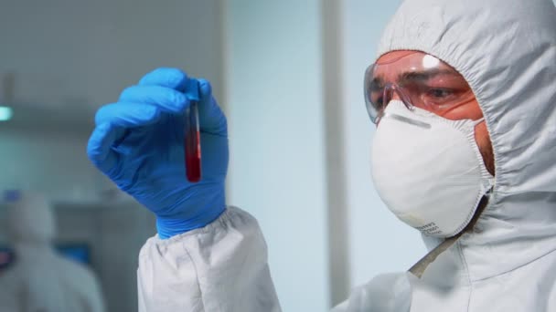 Cientista em macacão examinando tubos de teste de sangue em laboratório — Vídeo de Stock