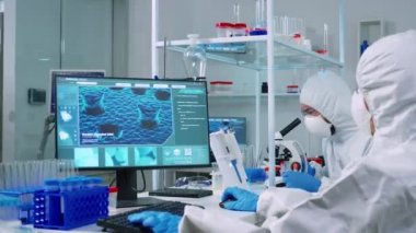 Kimyager mikroskop kullanırken PC giysili doktor bilgisayarda çalışıyor.
