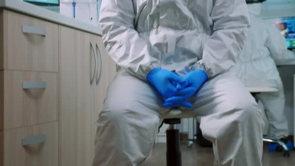 Dokter man kijkend naar camera zittend in lab gekleed in ppe pak — Stockvideo