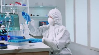 Pen Kostüm 'deki bilim adamı hemşire test tüpüne bakarak bilgisayarda notlar alıyor.