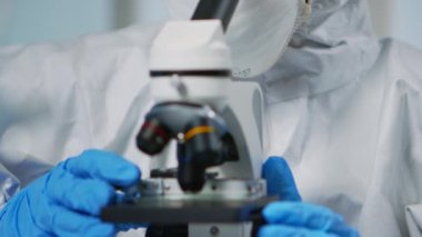 Kıyafetli deneyimli bir biyolog mikroskop üzerinde çalışıyor.