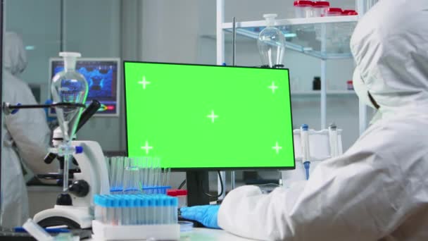 Доктор носить захисний костюм, друкуючи на комп'ютері з зеленим маком — стокове відео