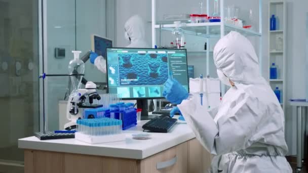 Chemik v kombinéze kontroluje krevní vzorky a dělá si poznámky na počítači — Stock video