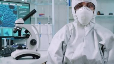 Laboratuvarda takım elbiseli bir mikrobiyolog kameraya bakıyor.