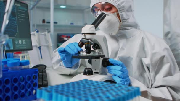 Scienziato indossando tuta ppe guardando i campioni al microscopio — Video Stock
