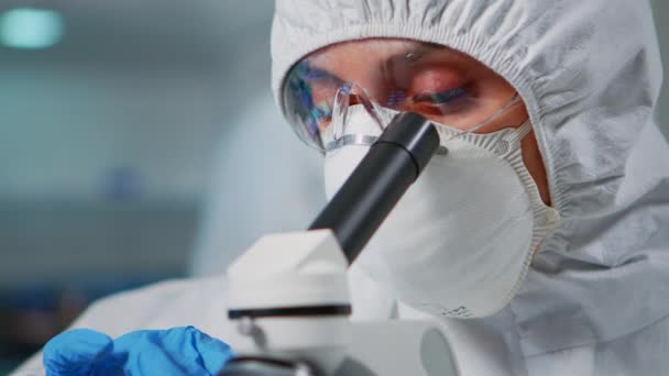Tecnico di laboratorio con tuta protettiva che esamina campioni utilizzando il microscopio — Video Stock