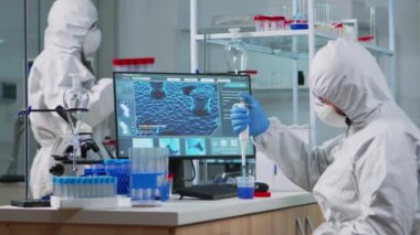 Mikro pipet doldurma tüpleri kullanan koruma giysisi giyen bilim adamı.