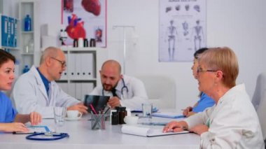 Personel toplantısındaki tıpçılar birbirlerinin önünde oturup konuşuyorlar.