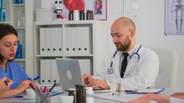 Laboratuvar önlüklü ve steteskoplu doktor kameraya bakıp gülümsüyor.
