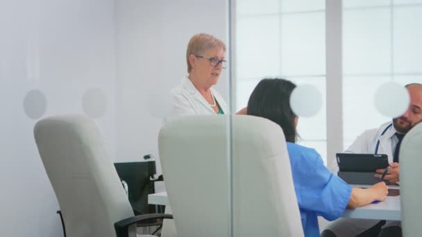 Läkarteam sitter och diskuterar vid bord på sjukhusets möteskontor — Stockvideo