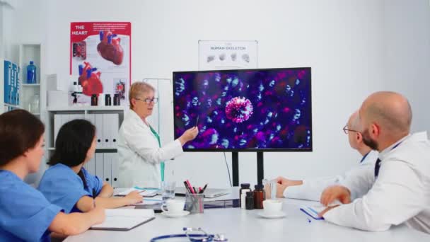 Starší zdravotník prezentující vývoj viru ukazující na displej v nemocniční kanceláři — Stock video
