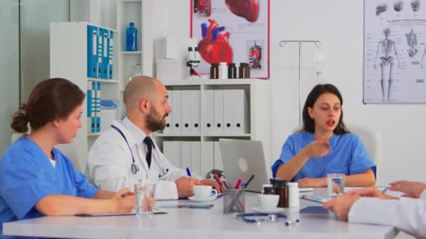 診察室の机に座ってブレインストーミング中の医師のチーム — ストック動画