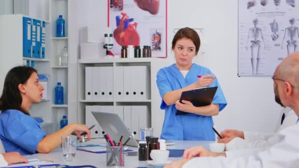 Équipe de médecins discutant du diagnostic assis à table à la clinique — Video