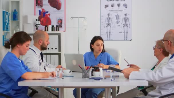 Enfermera sentada en la mesa de conferencias discutiendo con el equipo — Vídeos de Stock