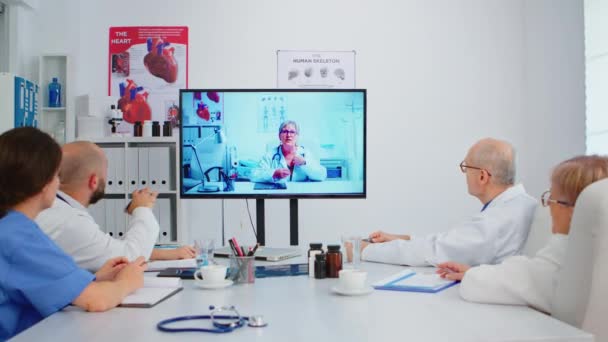 병원 회의실 책상에 앉아서 비디오 회의를 하고 있는 의사 팀 — 비디오