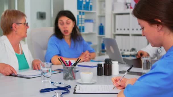 Nurse writing on clipboard while profesional teamworkers having medical meeting — Stock Video