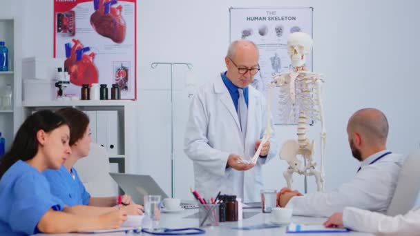 Senior man doctor presenting the work of humans hand on skeleton model — Stock Video