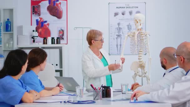 Пожилая женщина-врач показывает работу человека рукой на модели скелета — стоковое видео