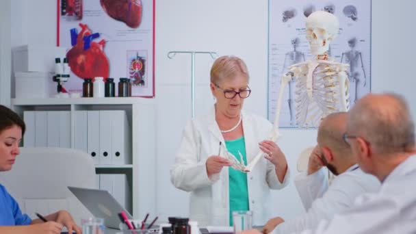 손 골격 모델을 들고 있는 선임 여성 의사 — 비디오