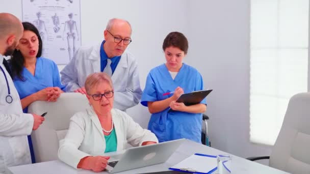 Médico practicante que trabaja en el ordenador portátil durante la reunión informativa con compañeros de trabajo — Vídeo de stock