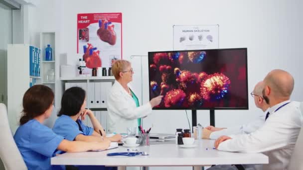 ウイルスの発生を説明する病院のモニターを指している上級医師 — ストック動画