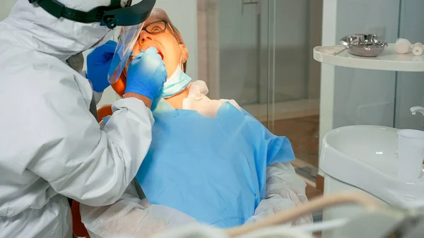 Técnico dentista em lâmpada de iluminação macacão para examinar paciente — Fotografia de Stock