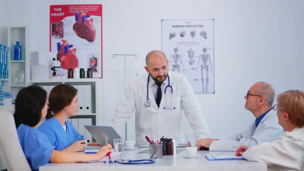 Профессиональный врач стоит перед коллегами и представляет медицинские отчеты — стоковое видео
