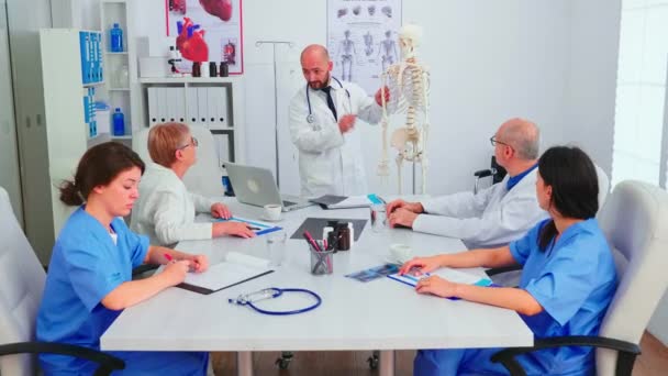 Médico explicando radiografía frente al personal médico usando esqueleto — Vídeo de stock