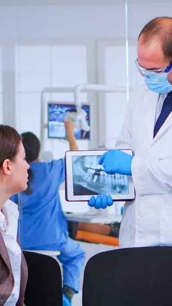 Woman sitting on chair listening doctor looking on tablet with x-ray