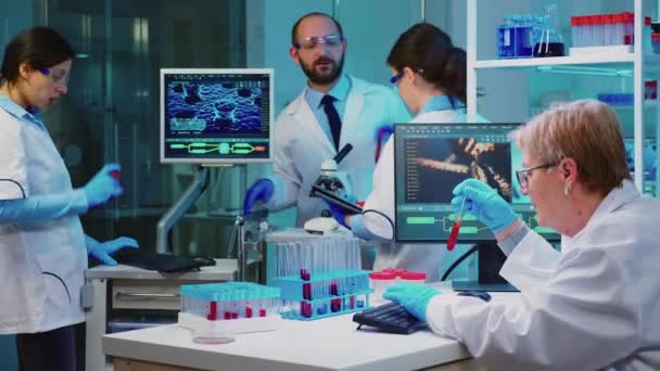Chefchemiker analysiert Blutprobe, während Mitarbeiter diskutieren — Stockvideo
