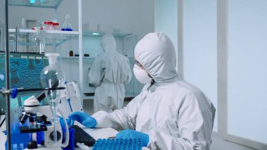 Pen kıyafetli bilim adamı virüs örneklerini incelerken elinde petri kabı tutuyor.
