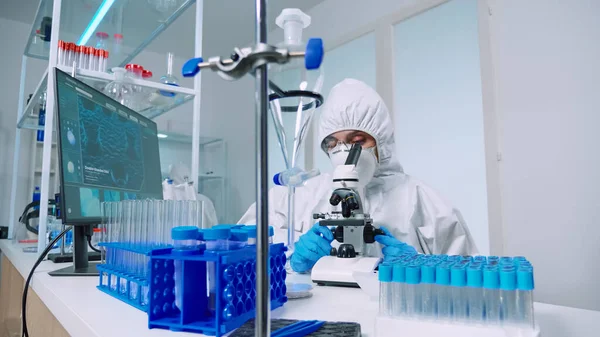 Cientista em terno de proteção conduzindo análise de vírus usando microscópio — Fotografia de Stock