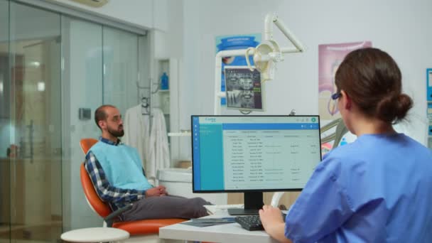 Assistentin verabredet sich, während Zahnarzt Mann untersucht — Stockvideo