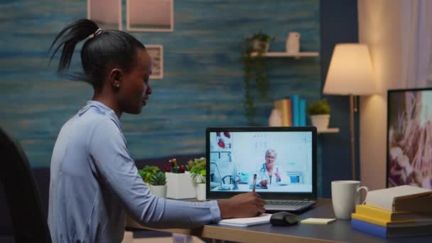 Mujer africana hablando en línea con el médico tomando notas durante tele salud — Vídeos de Stock