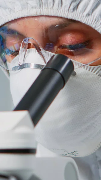 Лаборант с защитным костюмом, изучающий образцы с помощью микроскопа — стоковое фото