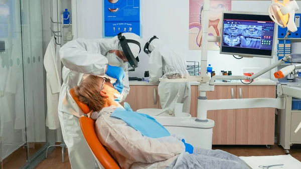 Dentista em terno de proteção examinando dentes com instrumentos médicos — Fotografia de Stock