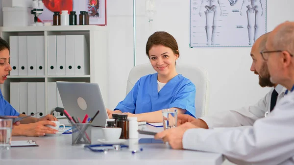 Krankenschwester schreibt während der Konferenz auf Laptop und blickt lächelnd in die Kamera — Stockfoto
