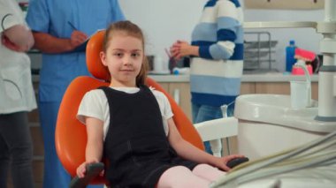 Pediatrik stomatolog bekleyen kameraya bakan küçük bir kızın portresi.