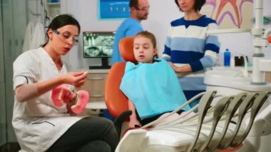 Stomatolog çocuğa çene kemiğinin alçı modelini kullanarak ameliyatı açıklıyor.